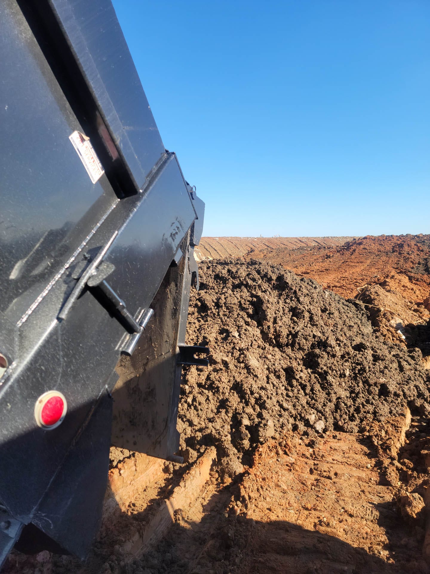 Close-up of a dump truck unloading a pile of soil onto a construction site, with a clear blue sky in the background.