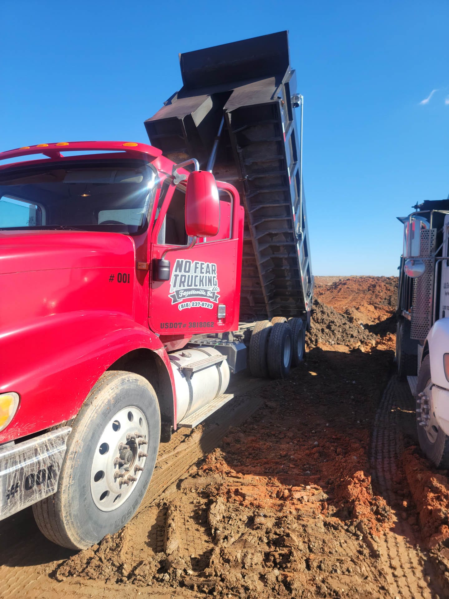 Red dump truck unloading dirt on a construction site under a clear blue sky.