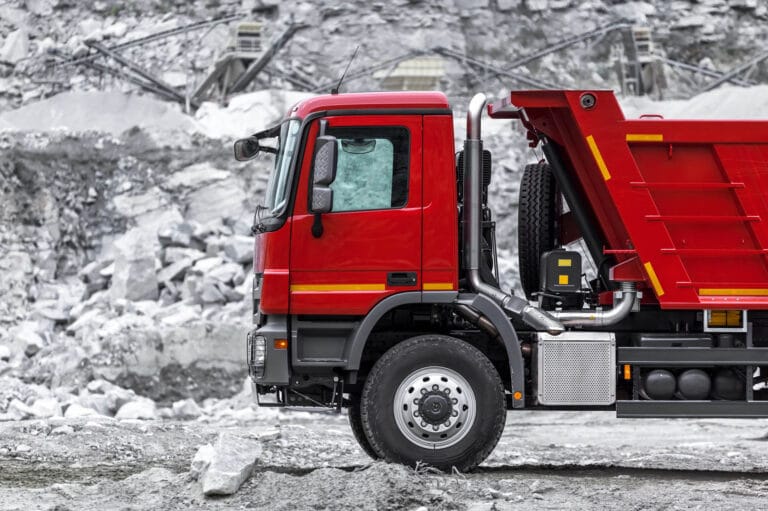 A red dump truck with a raised hopper stands proudly in a rocky quarry, all about rugged strength and reliability.