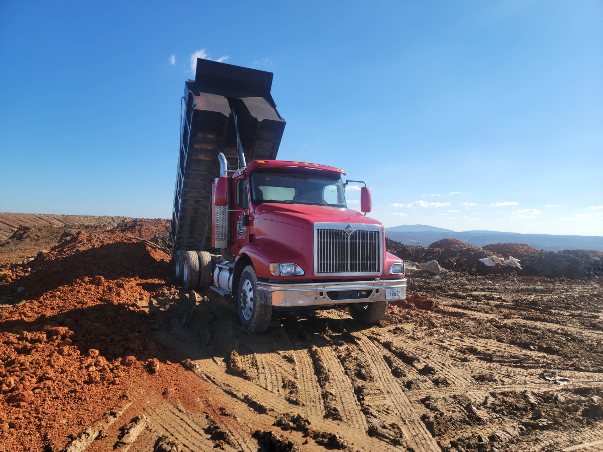 A red dump truck unloading dirt on a construction site under a clear blue sky.